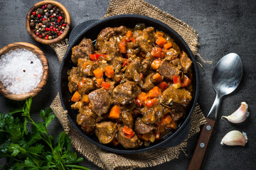 Beef stew with vegetables in iron pan on black.