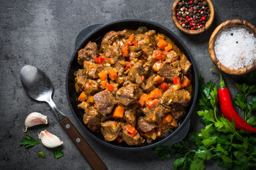 Beef stew with vegetables in iron pan on black.