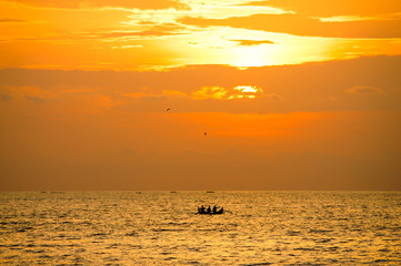 Fototapeta na wymiar Silhouette of three fishermen in a boat against the setting sun