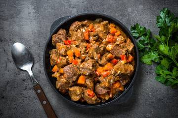 Beef stew with vegetables in iron pan on black.