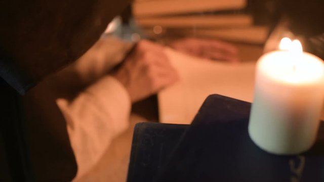 Big Close-up girl magician in a dark room with candlelight looking for a spell in a book. Low key live camera. Mystic. Small DOF