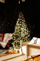 Christmas decor. Living room in loft style with a huge beautifully decorated Christmas tree with garlands and toys, under which there are boxes with gifts. Next to a red leather sofa and a cozy chair.