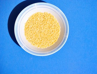Dry stars shaped pasta in the white bowl on the blue textile background.