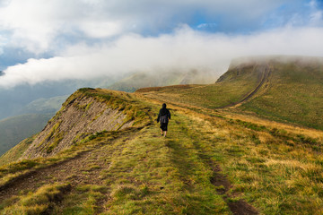 Obraz premium Young woman in black in the mountains at background of big clouds