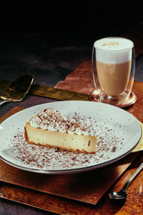 cheesecake and cappuccino. Cheesecake with cream top and chocolate chips on a white plate on a copper background. Close up