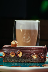 Brownie cake with whole nuts and cappuccino. Chocolate cake with hazelnuts on a blue plate on a background of copper plates. Close up