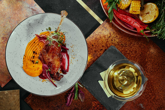 Duck leg with pumpkin puree, berry sauce and soy sprouts on a white plate on a copper background, served with white wine. top view. flat lay. close-up. a series of photos