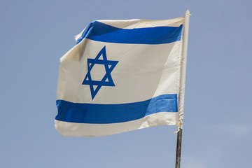 A tattered Israeli Flag aloft in a stiff breeze against a blue sky