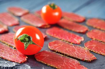 Close-up of meat slices with spices and tomatoes on a board with wooden table