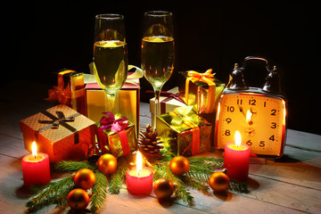 Glass of sparkling shampagne wine, clock, gift box and candles on christmas background.