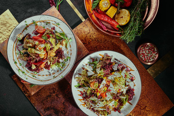 Salad with pomegranate, corn, tomatoes, arugula, parmesan cheese and cranberries and grilled vegetables salad on a white plates on a copper background. flat lay. top view. Close-up