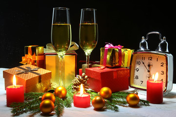 Glass of sparkling shampagne wine, clock, gift box and candles on christmas background.