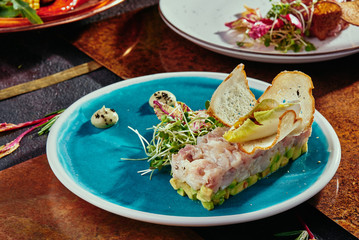 Delicious salmon tartare with toasted bread and salad on a blue plate on a copper background. Healthy lunch meal made of raw salmon. Classical French cuisine.