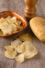 Potato chips on a bowl with raw potato and pepper grinder over white background
