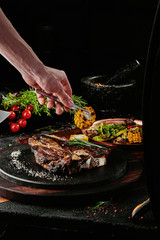 Fermented steak. T-Bone steak serving with grilled vegetables on a black round plate on a background of greens, spices and vegetables, on a copper sheet. close up