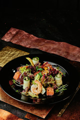 Salad with salmon, shrimps, lettuce, cucumber and soybean sprouts in a black plate on a background of copper plates. close up