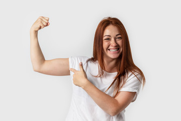 Portrait smiling woman in white t-shirt , isolated on gray background. Showing biceps muscle having...