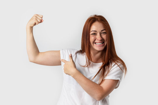 Portrait smiling woman in white t-shirt , isolated on gray background. Showing biceps muscle having lifted arm with clenched fist
