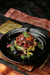 salad with veal, grilled vegetables, sprouts and lettuce leaves on a black plate on a copper background
