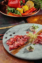 cold smoked meat plate with thin slices of meat, white sauce and soybean sprouts on a marble plate on a copper background on the background of grilled vegetables. close up