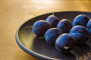 juicy blue plums in ceramic plate on wooden background