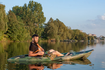 Young bearded man sitting in kayak in the middle of the lake