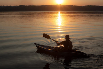 A man with paddle on kayak silhouette in sunset, from the left side