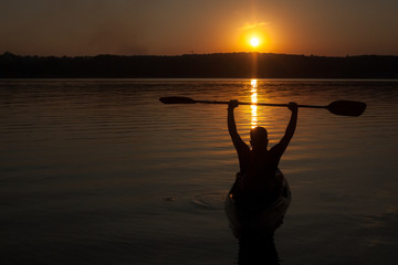 A man with paddle in his hands on kayak silhouette in sunset, look from the back