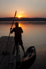 A man silhouette with paddle standing near kayak in sunset