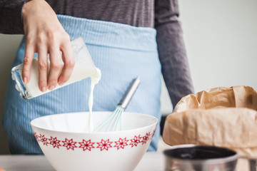 Young woman adding a milk to the egg mixture.making dough for the cake. selective focus.