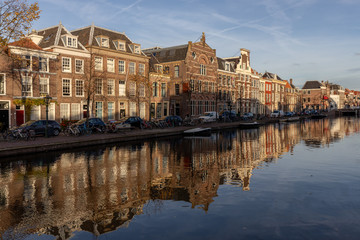Autumn picturesque view on an old part of the city Leiden with classic facades against a blue sky with the scene doubled as a reflection in the water of the passing canal