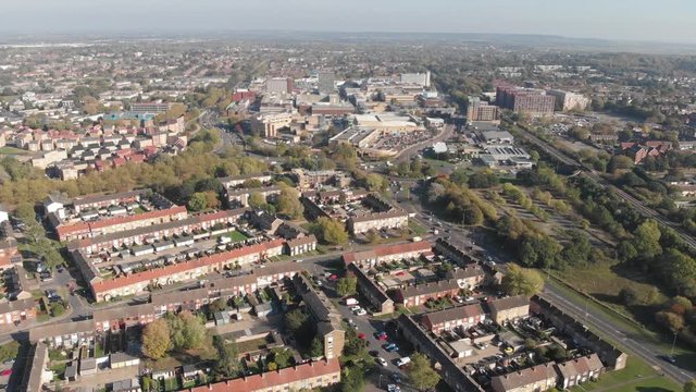 Flying over a residential area comprising of modern English houses on an autumn sunny day and the Basildon city center in the distance