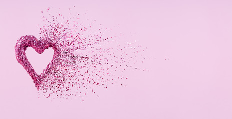 Glitter heart dissolving into pieces on pink background.  Valentines day, broken heart and love...