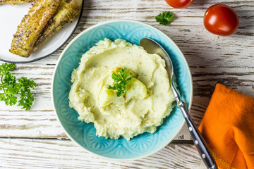 Mashed cauliflower with oil in blue bowl on wooden table.