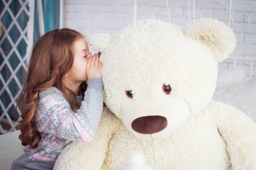 A child is played with a big teddy bear. A girl whispers in the ear of a bear. A fictional friend.
