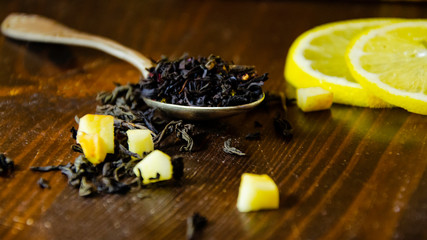 Dry tea leaves in a teaspoon, lemon, wooden table