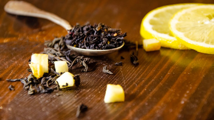 Dry tea leaves in a teaspoon, lemon, wooden table