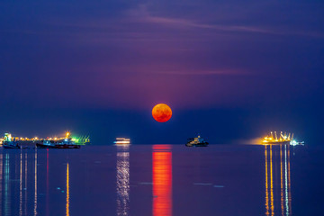 Super blood moon over Sriracha harbor with vessel cargo container ship on the sea water surface ....