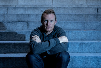 Obraz premium Depressed sad young man crying sitting on stairs feeling miserable lonely in urban scene