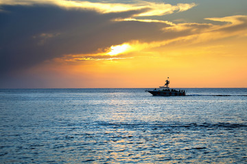 Colorful seascape image with shiny sea and speedboat over cloudy sky and sun during sunset in Cozumel, Mexico