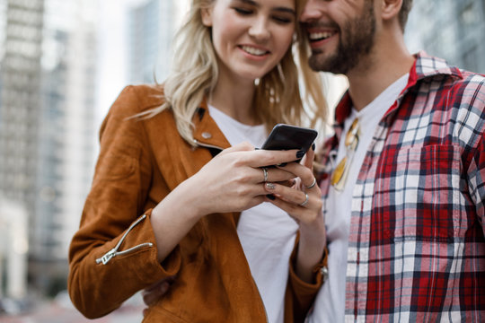 Low angle of cheerful young man and woman typing on handy screen