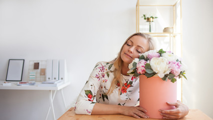 Happy blonde woman in a modern office with flowers in a hat box. Bouquet of peonies.