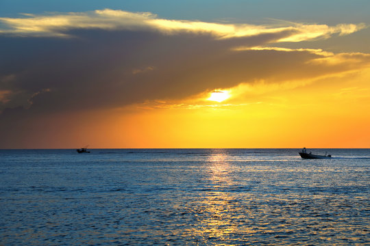 Colorful seascape image with shiny sea and speedboat over cloudy sky and sun during sunset in Cozumel, Mexico