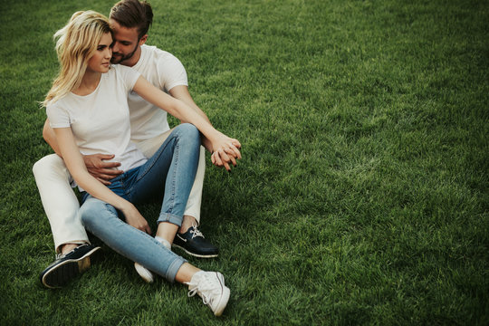 Happy couple is sitting on grass and hugging. They holding hands. Copy space on right side