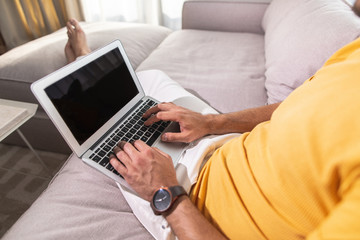 Fototapeta premium Adult male is siting on sofa and working with laptop