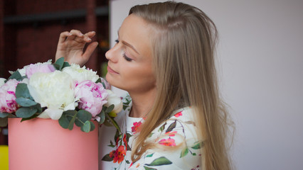 Happy blonde woman in a modern office with flowers in a hat box. Bouquet of peonies.