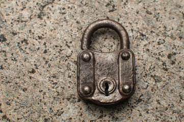 Old weathered grunge retro locked padlock closeup on solid stone surface background