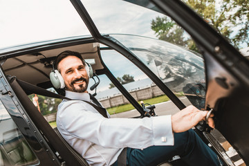 Emotional confident pilot sitting in the helicopter and smiling while opening the door of the cabin