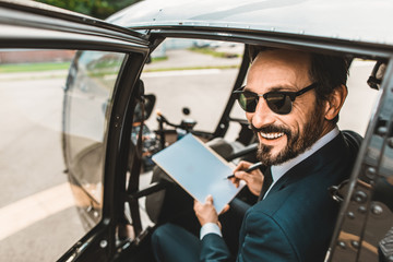 Cheerful bearded young man sitting in the helicopter and smiling happily while holding his documents © Yakobchuk Olena