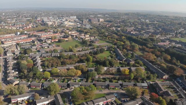 An aerial view of a residential area comprising of modern English houses surrounding a woodland area on an autumn sunny day and the Basildon city center in the distance